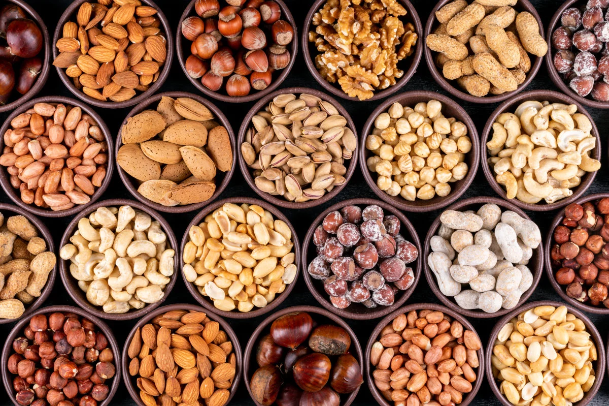 Set of pecan, pistachios, almond, peanut, cashew, pine nuts and lined up assorted nuts and dried fruits in a mini different bowls on a black stone background. flat lay.