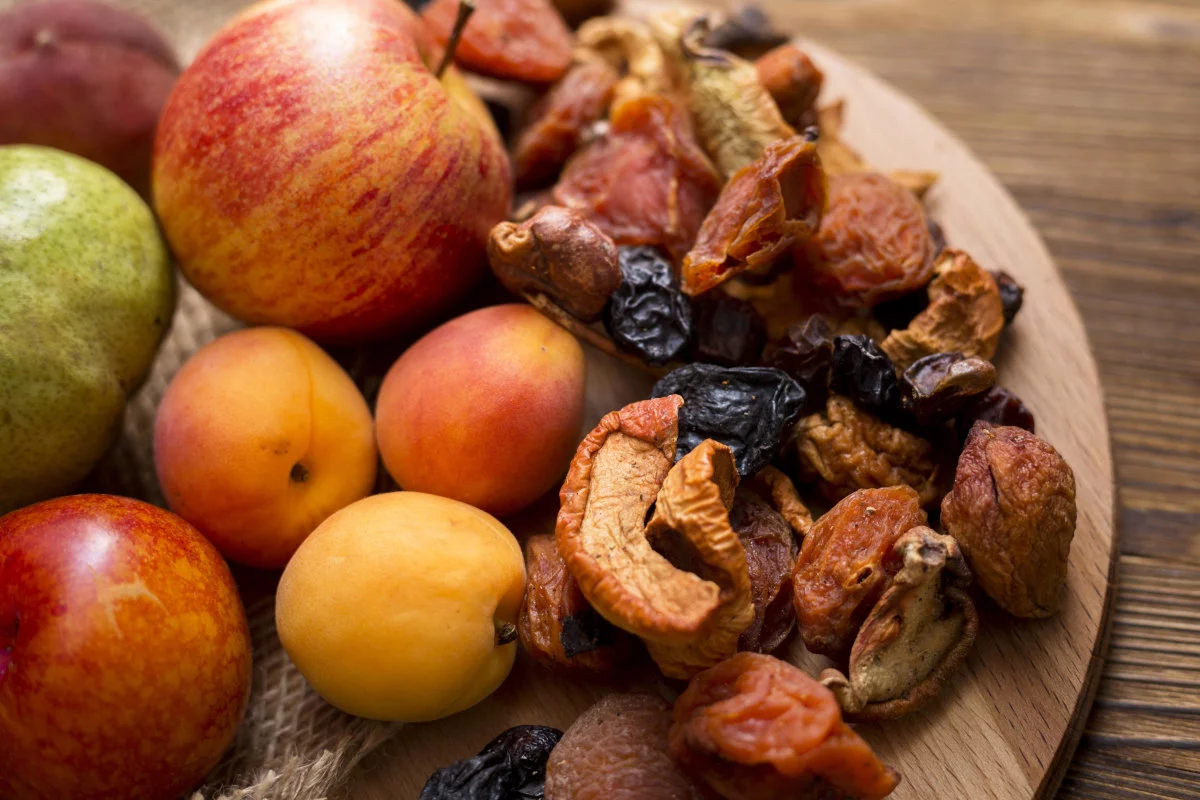 Limmagine mostra unampia selezione di frutta fresca come mele, pere, albicocche e prugne, affiancata da un grande mucchio di frutta secca varia, il tutto su una tavola di legno.